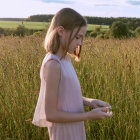 Young girl in light dress standing in golden wheat field at sunset