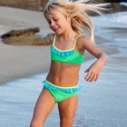 Young girl in turquoise swimsuit playing at the beach with splashing water droplets