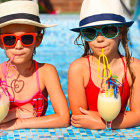Stylized individuals in colorful sunglasses and white hats eating sweets under surreal blue sky
