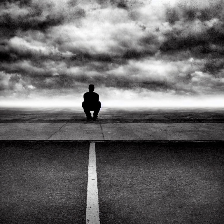 Person sitting on empty road under dramatic cloudy sky