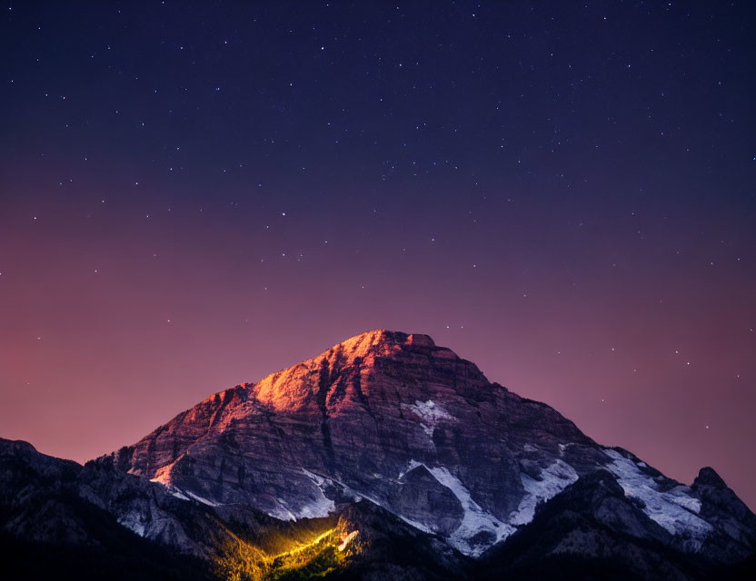 Mountain Peak Illuminated by Warm Glow Against Starry Night Sky