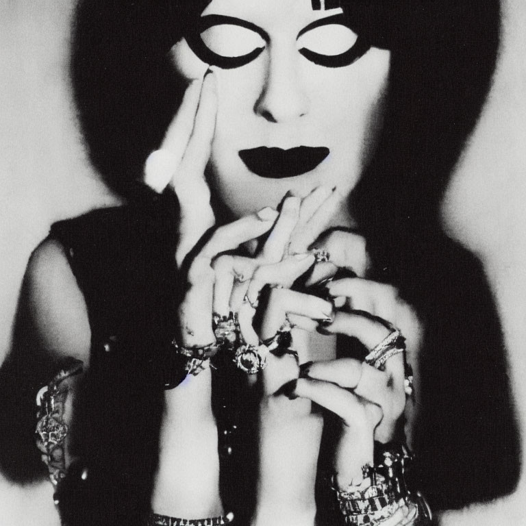Monochrome portrait of person with striking eye makeup and rings, touching face dramatically