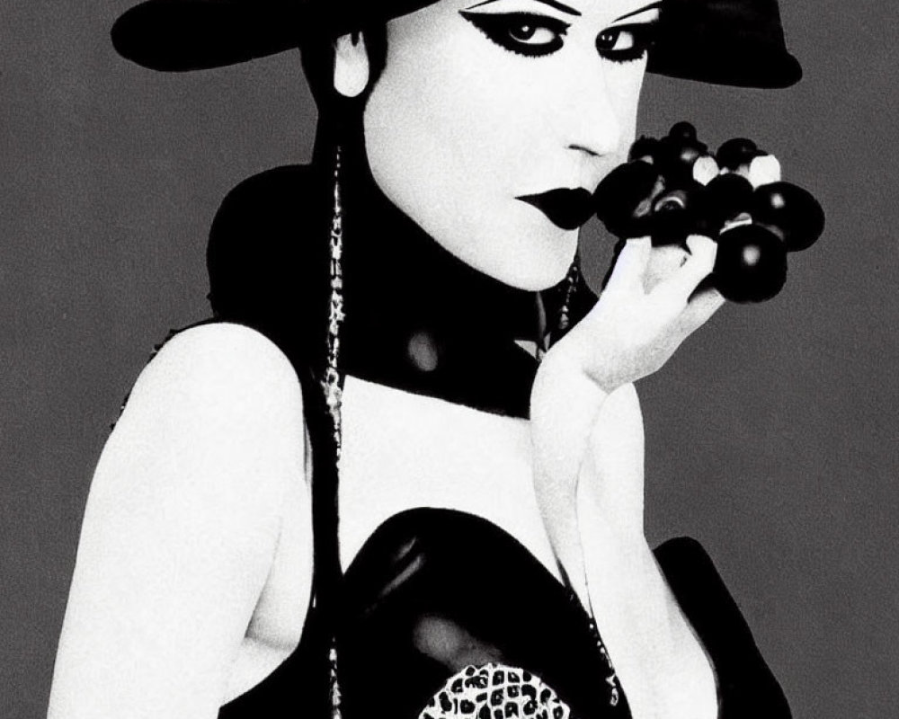 Monochrome image of woman with dark makeup and wide-brimmed hat holding grapes