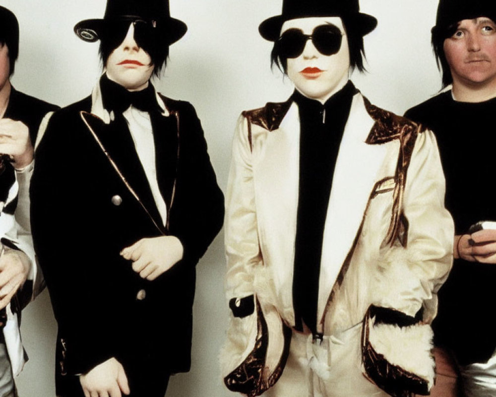 Group of four individuals in eclectic formal attire with top hats, two in black suits and sunglasses, two
