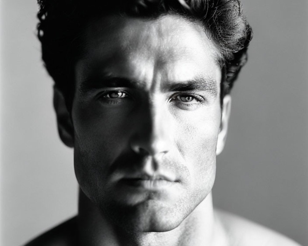 Intense monochrome portrait of shirtless man with wavy hair and strong jawline