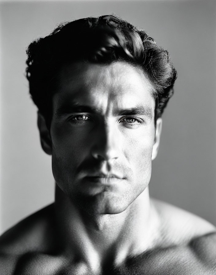 Intense monochrome portrait of shirtless man with wavy hair and strong jawline