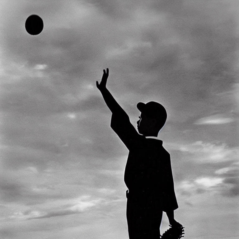 Child silhouette with baseball cap and glove reaching for ball in cloudy sky