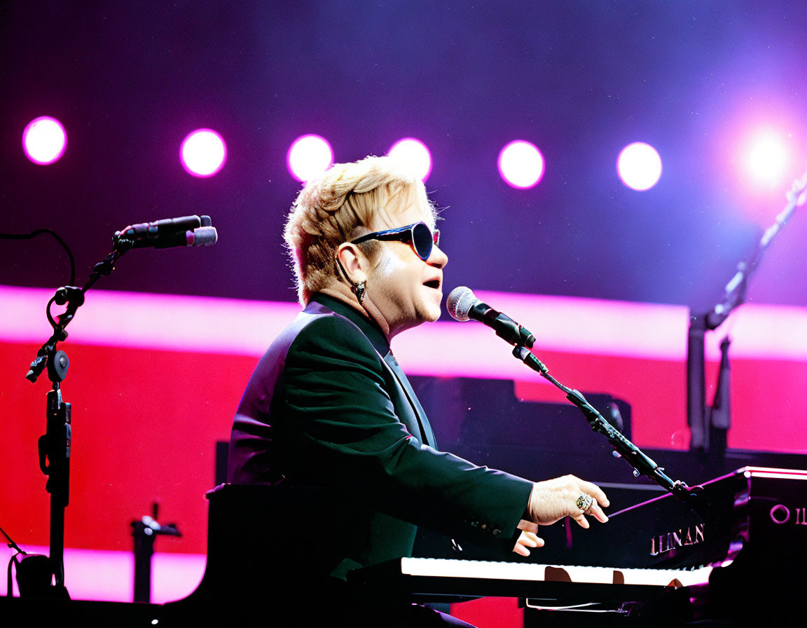 Musician in sunglasses and suit performing at piano under purple stage lights