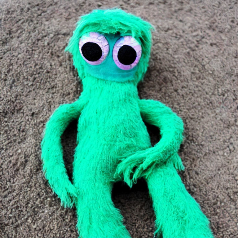 Green Plush Toy with Pink and White Eyes on Sand Surface