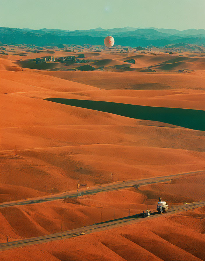 Desert road scene with truck, sand dunes, settlement, and setting sun
