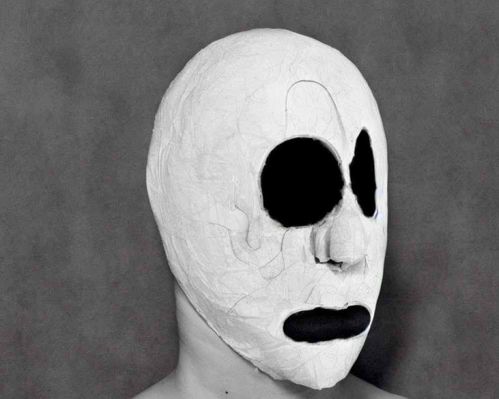 White Textured Mask with Asymmetric Black Eye Holes and Mouth Opening on Grey Background