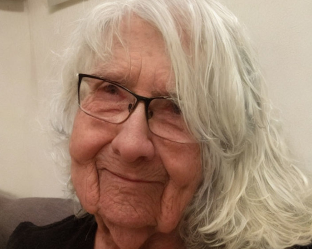 Elderly lady with glasses and white hair smiling indoors with watermark