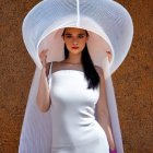Dark-haired woman in white sunhat and dress against earthy background