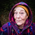 Person with facial markings and tribal jewelry in purple hood in mystical forest