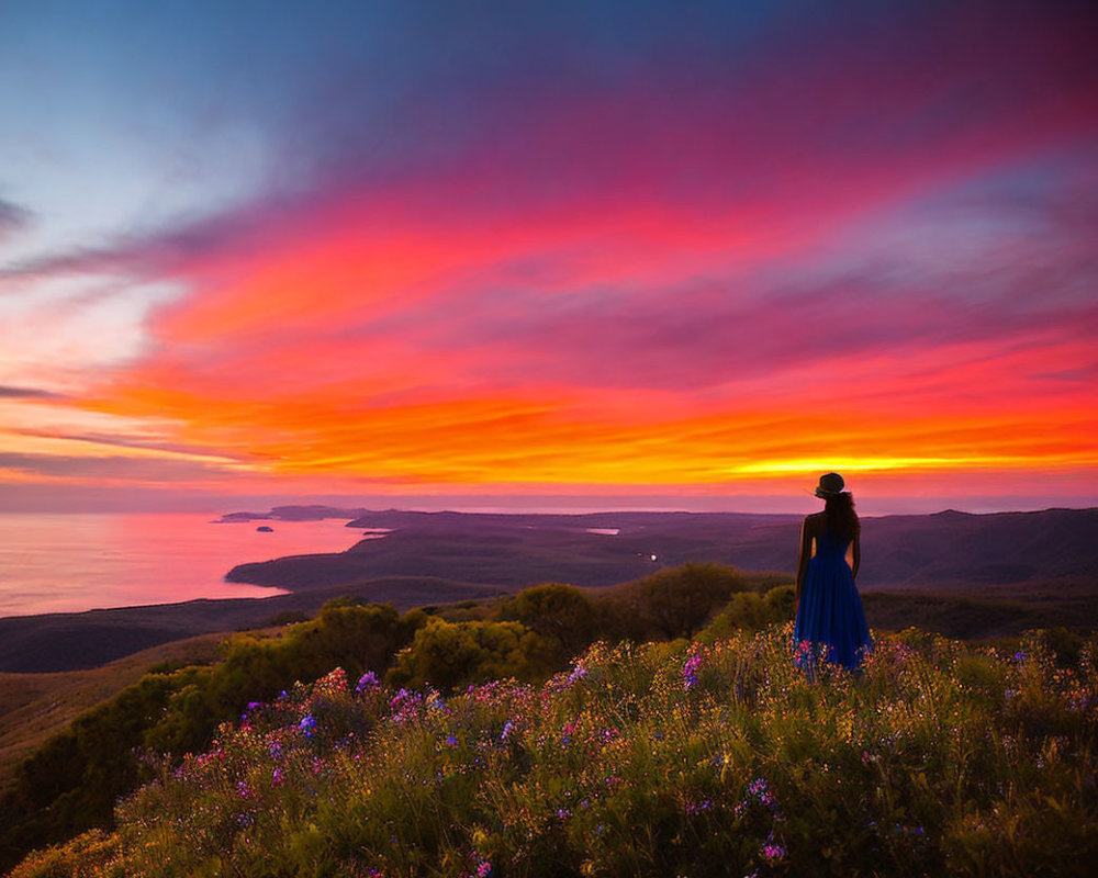 Person in Blue Dress Surrounded by Wildflowers at Vibrant Coastal Sunset