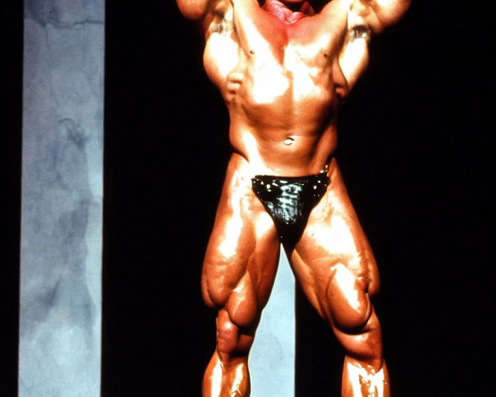 Muscular bodybuilder flexes muscles in black posing trunks