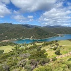 Scenic panoramic view of vibrant blue lake, green forests, and rocky terrain under dynamic sky