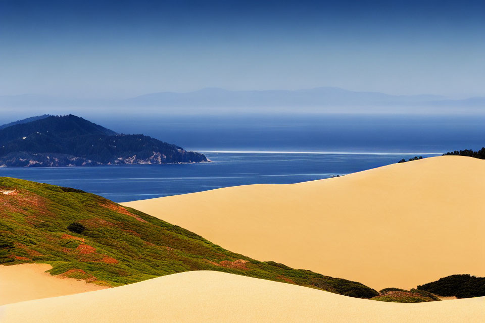 Coastal sand dunes, green vegetation, calm sea, mountains, clear sky