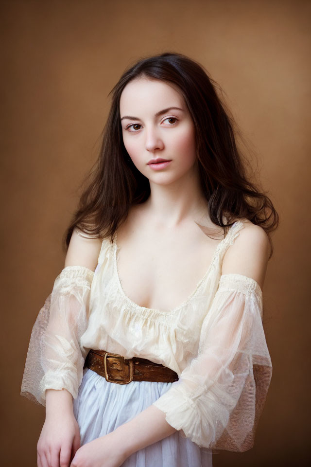 Young woman with long dark hair in white blouse and brown belt against golden backdrop