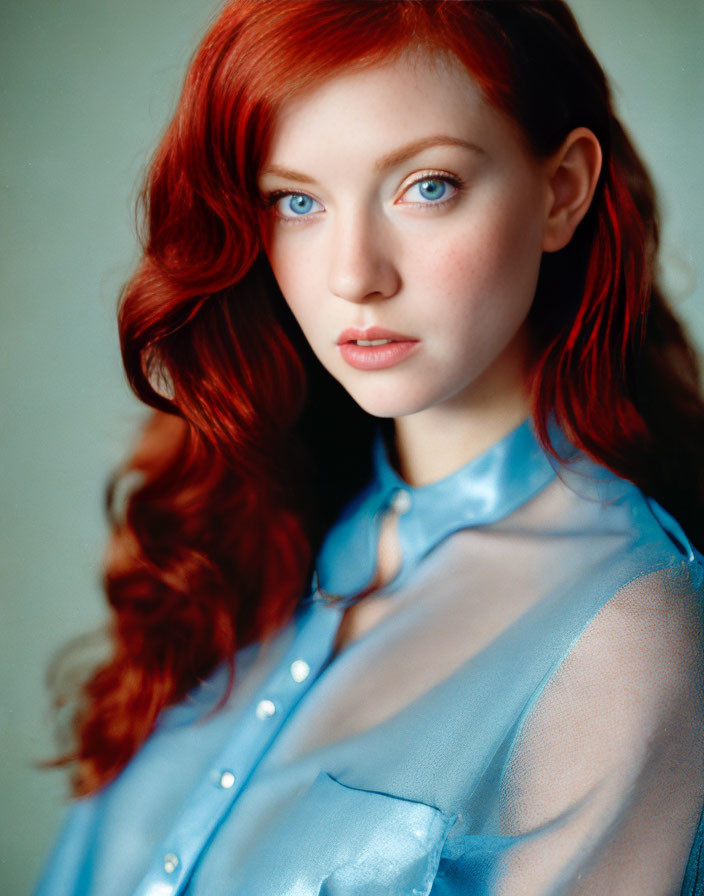 Portrait of a woman with red hair and blue eyes in a sheer blue blouse