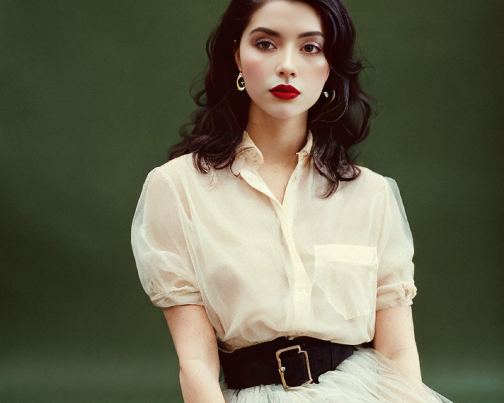Dark-haired woman in sheer blouse and tulle skirt with red lipstick on green background