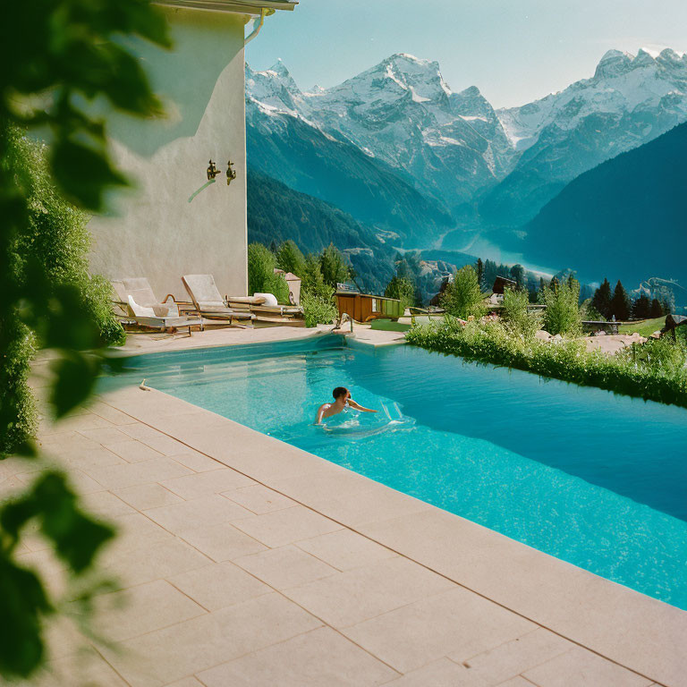 Swimmer in outdoor pool with snow-capped mountains and blue skies
