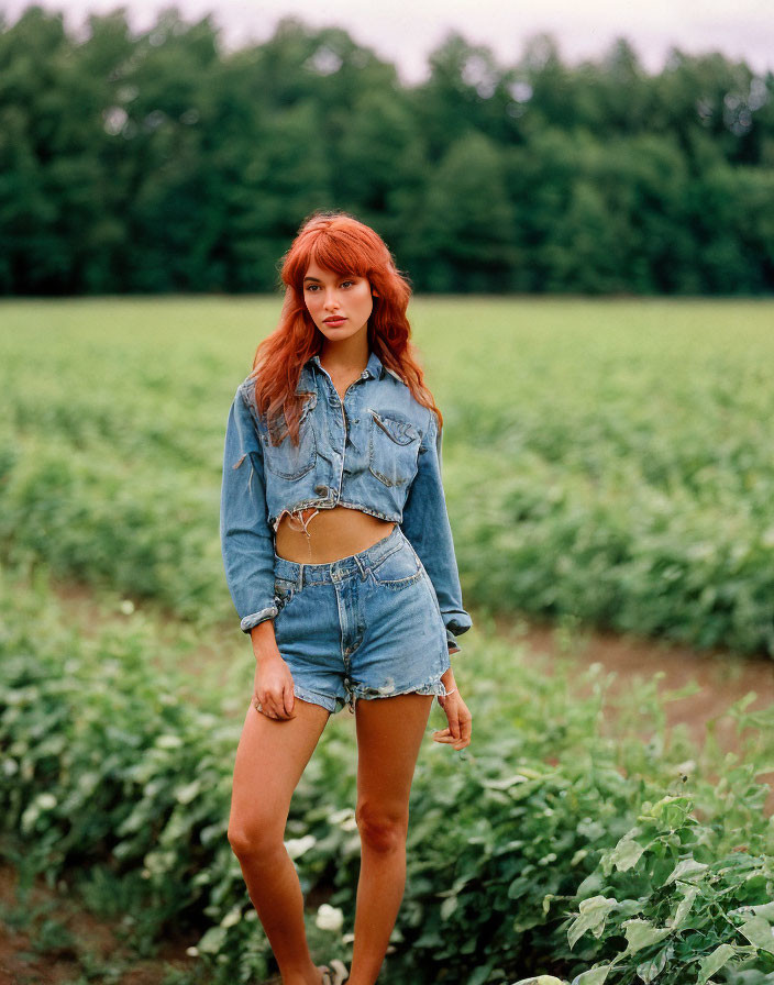 Red-haired woman in denim jacket and shorts standing in field.