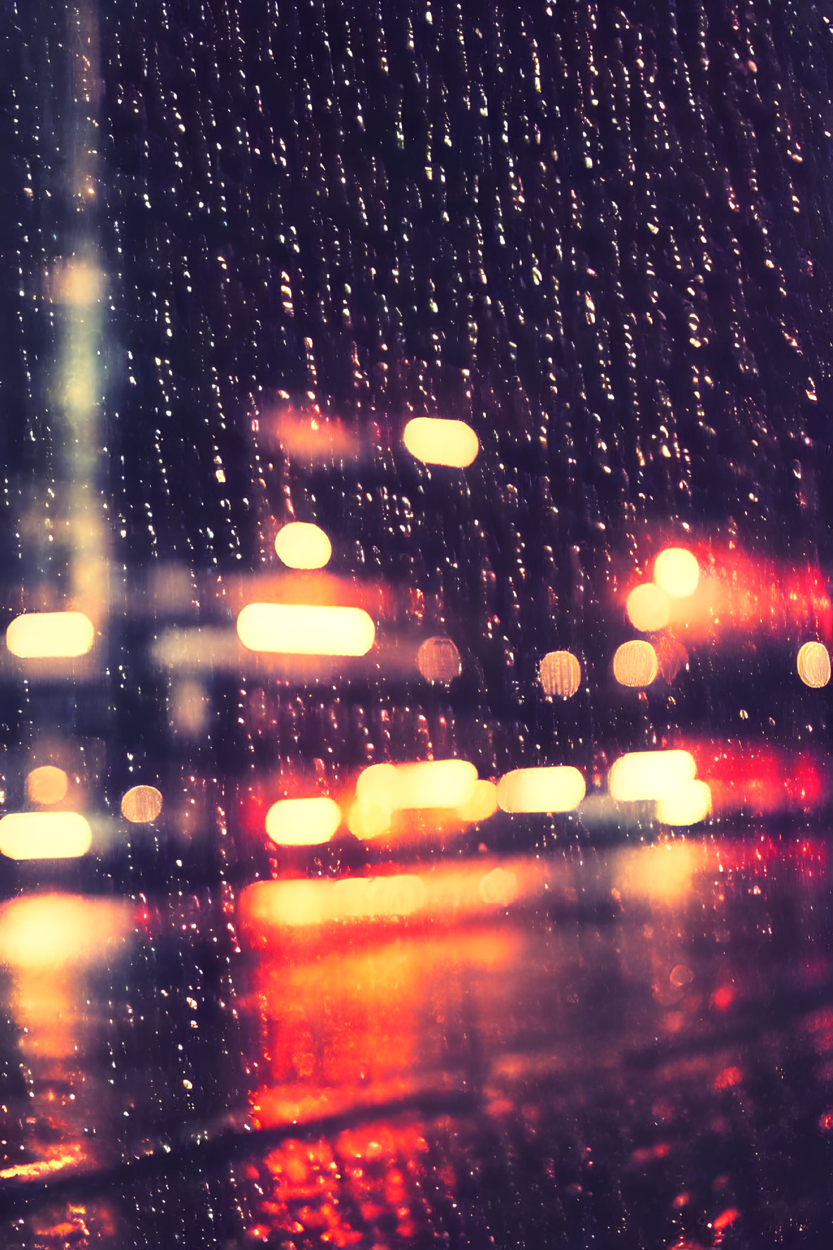 Raindrops on window with colorful city traffic bokeh lights at night