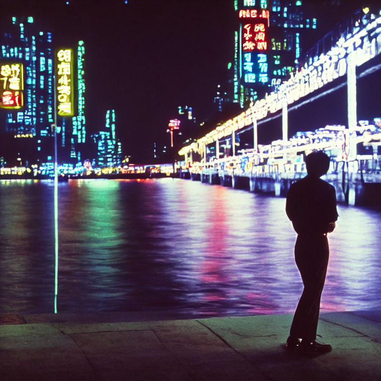 Silhouette of person by waterfront at night with city lights reflecting on water