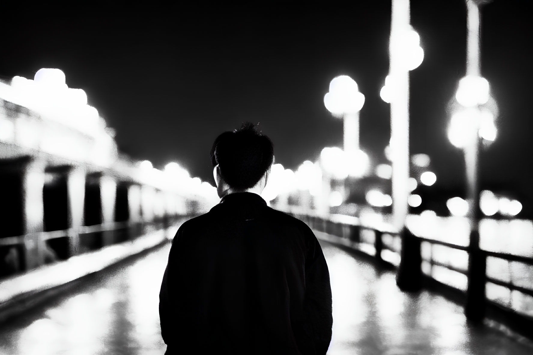 Monochrome image of person gazing at brightly lit bridge at night