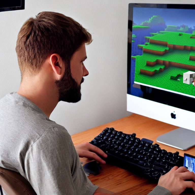 Bearded man using computer with Minecraft game and holding smartphone