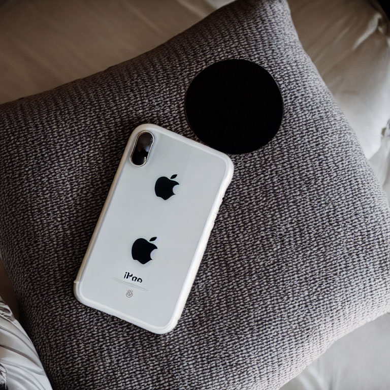 White Smartphone with Apple Logo on Gray Pillow Next to Black Object