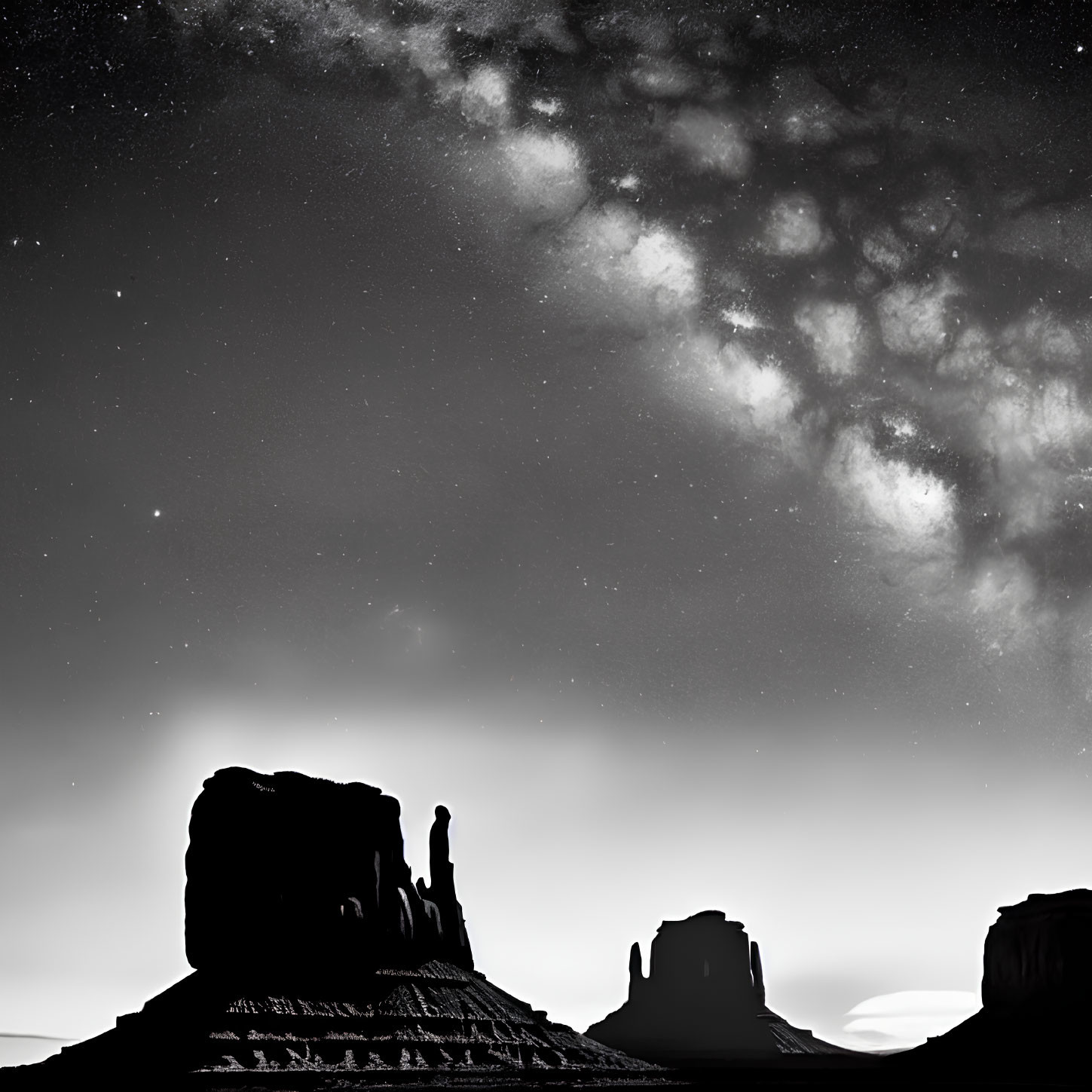 Monochrome image of starry sky over silhouetted rock formations