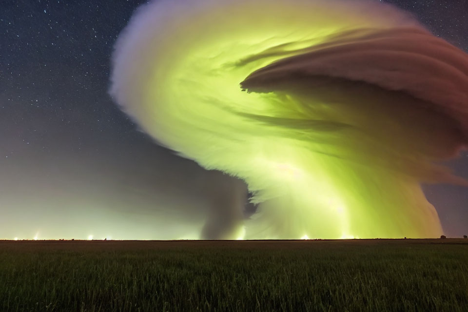 Gigantic supercell thunderstorm over night field with green light and starry sky