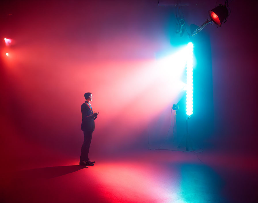Person in Suit Stands on Stage with Dramatic Lighting and Device