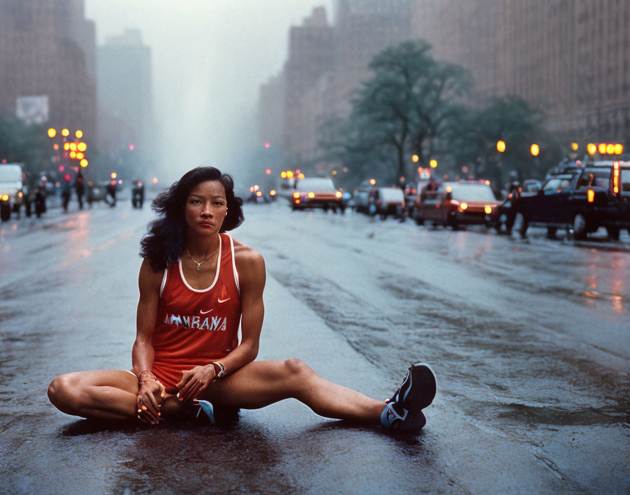 Woman stretching on wet city street with blurred traffic and cityscape.
