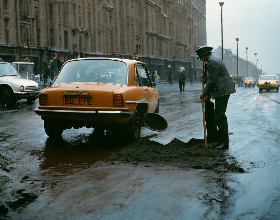 Man shoveling wet asphalt near orange car on rainy day by historical buildings