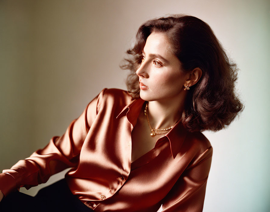 Woman in satin blouse and pearl earrings with shoulder-length hair on soft background