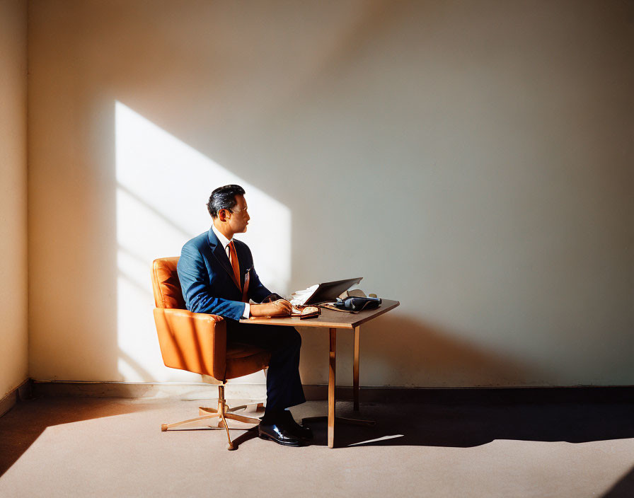 Businessman working on laptop in sunlit room with geometric shadow.