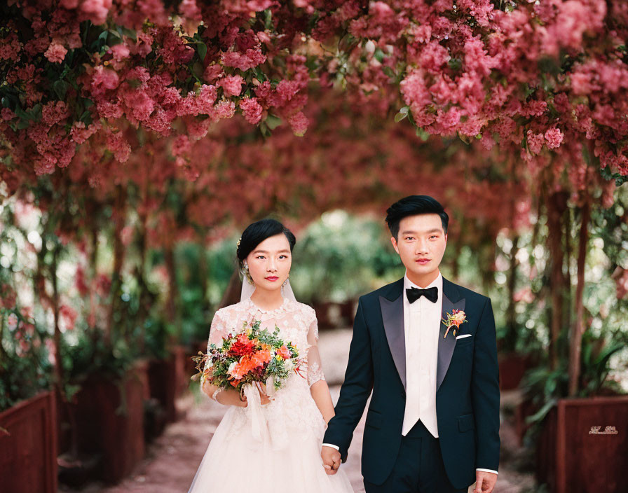 Wedding couple holding hands under pink flower archway