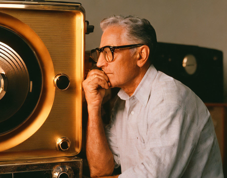 Elderly man with glasses gazing at vintage wooden speaker