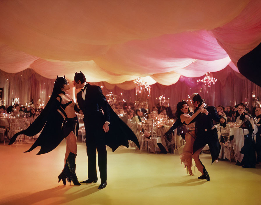 Two people in Batman costumes dance at formal event with seated onlookers.