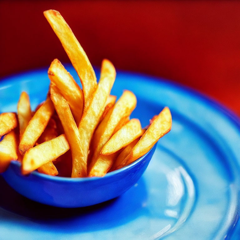 Crispy golden French fries in blue bowl on red background