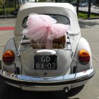 Vintage car adorned with large pink bow and colorful confetti