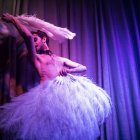 Graceful dancer in white and pink fan costume under purple lighting