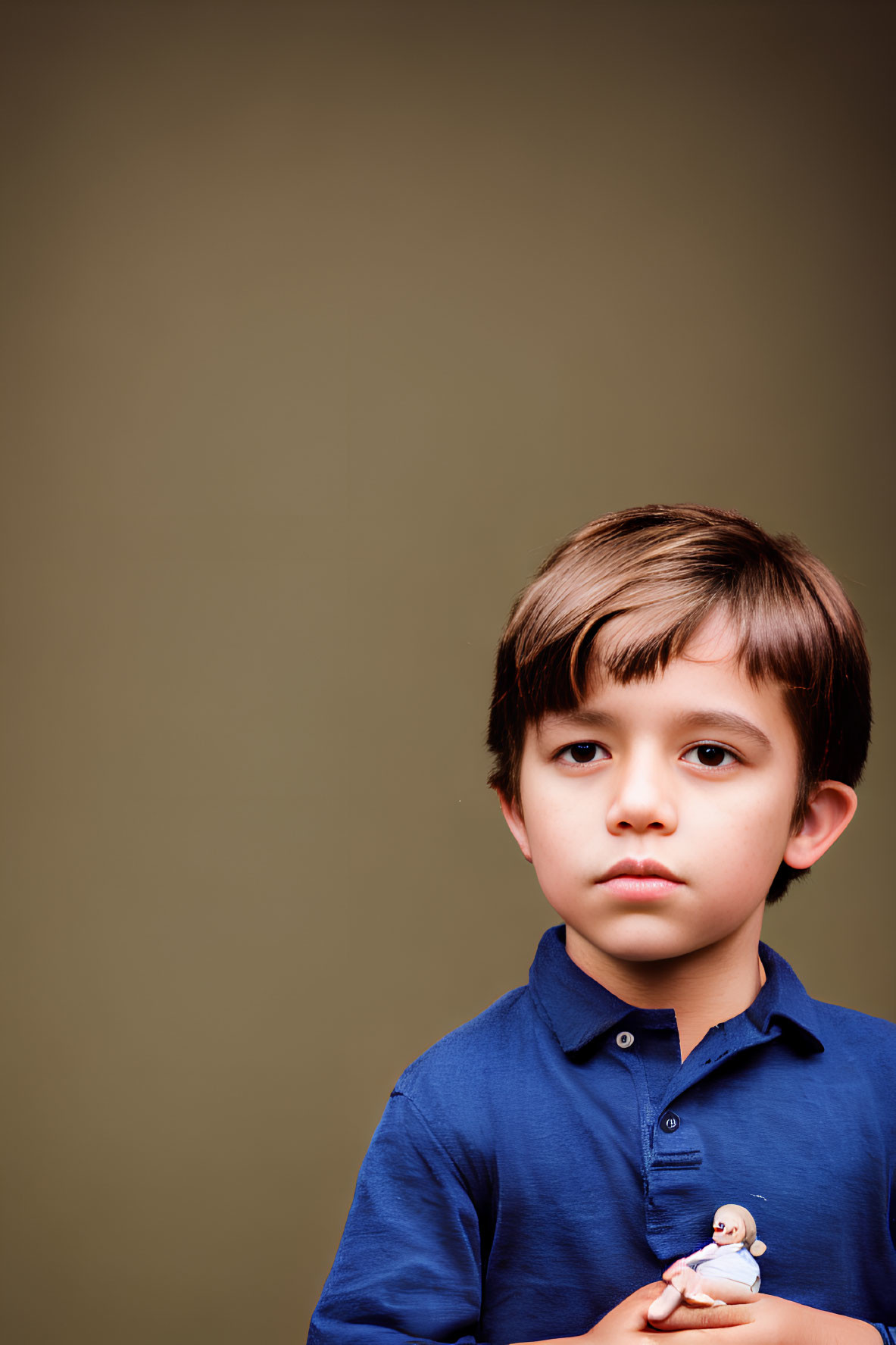 Young boy in blue shirt holding figurine on brown background