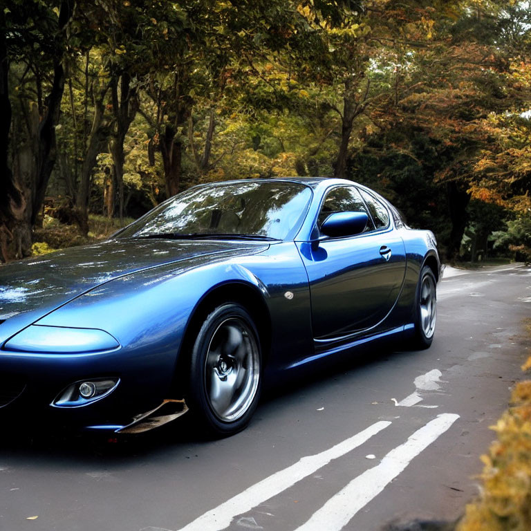 Blue sports car parked on tree-lined road with autumn leaves - serene scene.