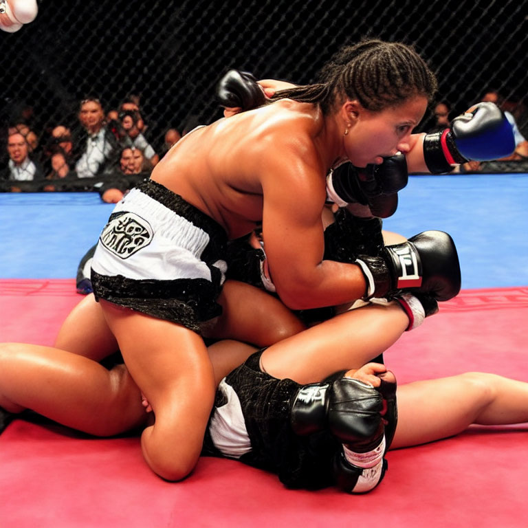Female MMA fighters in grappling position on red mat, one in dominant black and white shorts.