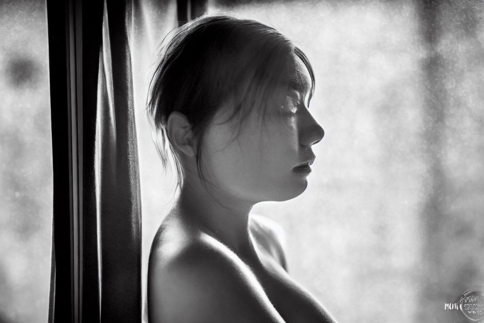 Monochrome profile portrait of woman in contemplative pose with soft window light