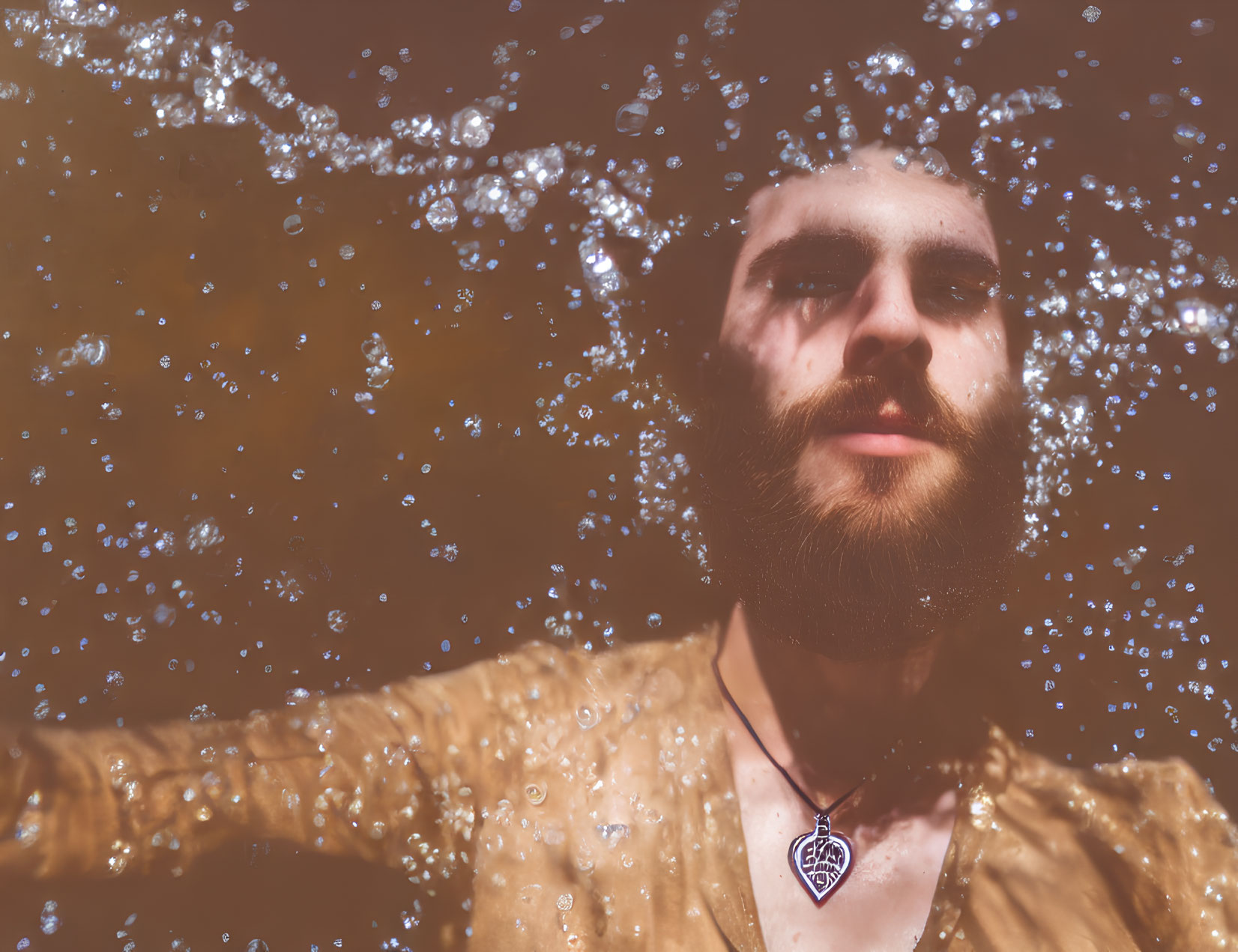 Man with beard in water, bubbles, necklace, yellow shirt, serene expression
